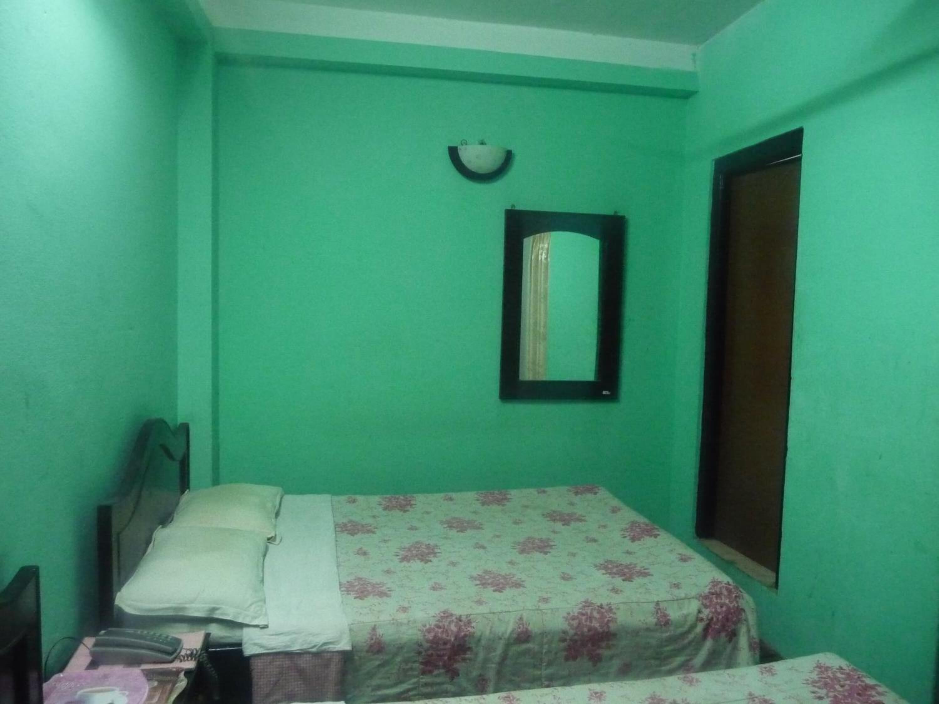 Une petite chambre avec un lit simple, un mur vert, une table de chevet, un miroir et une fenêtre.