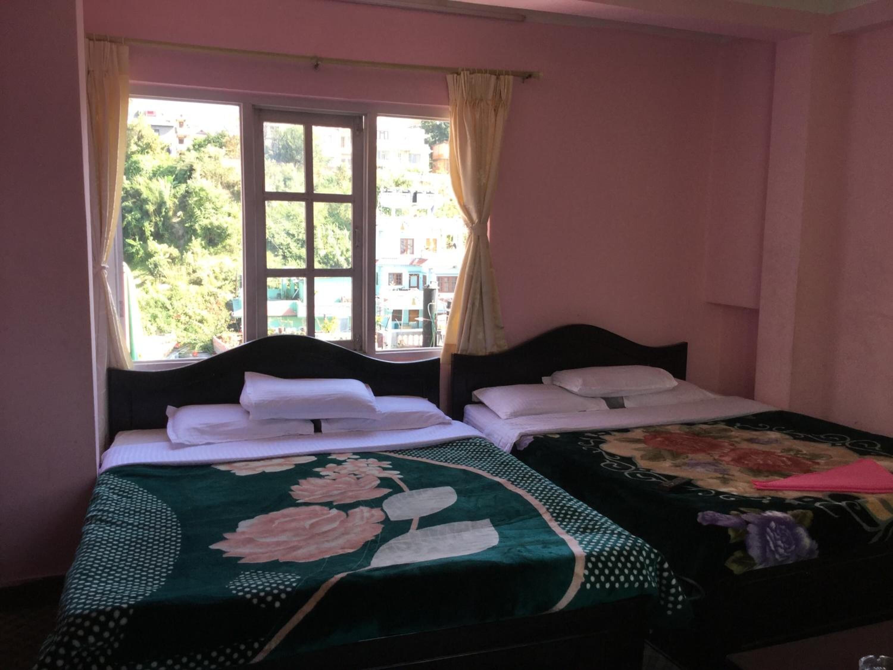 Una habitación con dos camas, cada una con colcha estampada, una ventana con cortinas y vistas al exterior con vegetación.