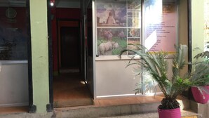 Entrada de hotel con puerta de vidrio, un cartel que muestra varios servicios y una planta en primer plano.