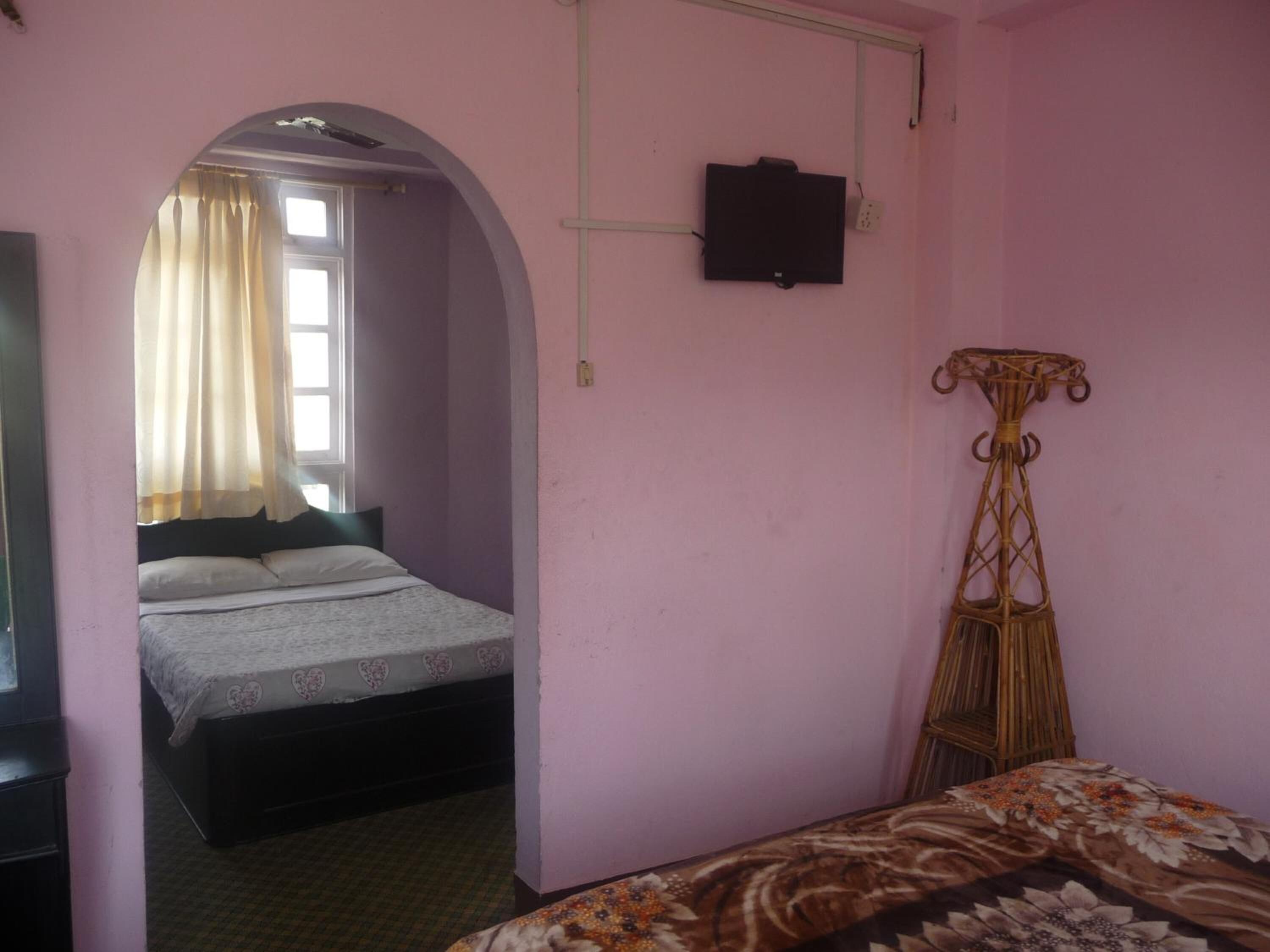 A bedroom with a bed, a television mounted on the wall, and a window with curtains.