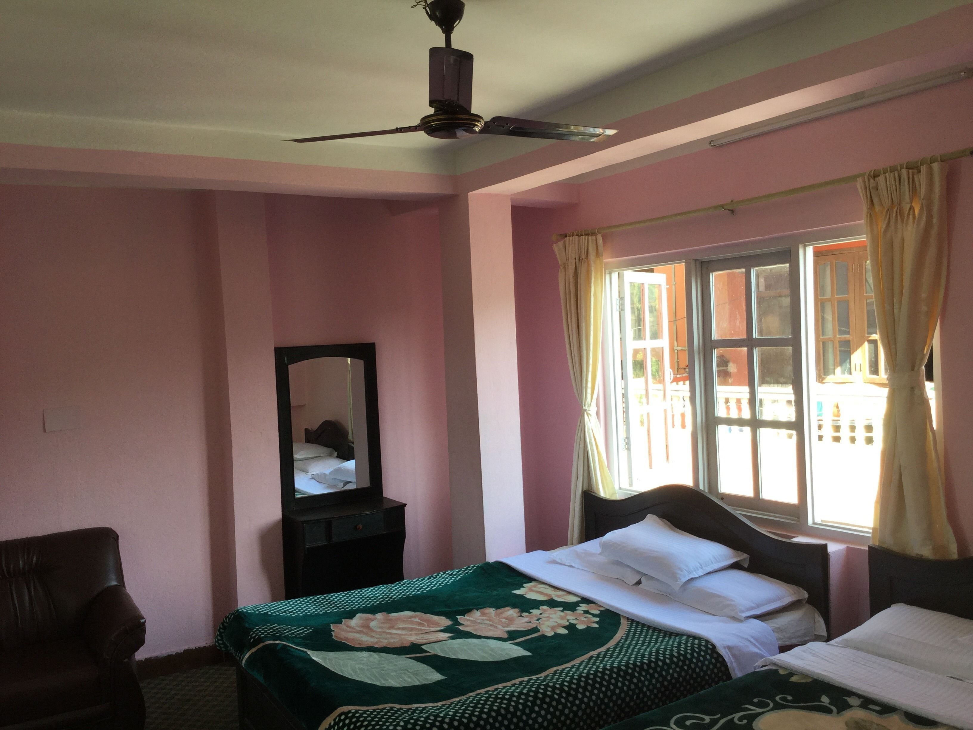 A bedroom with pink walls, a bed with a floral bedspread, a dresser, a mirror, and a window with curtains.