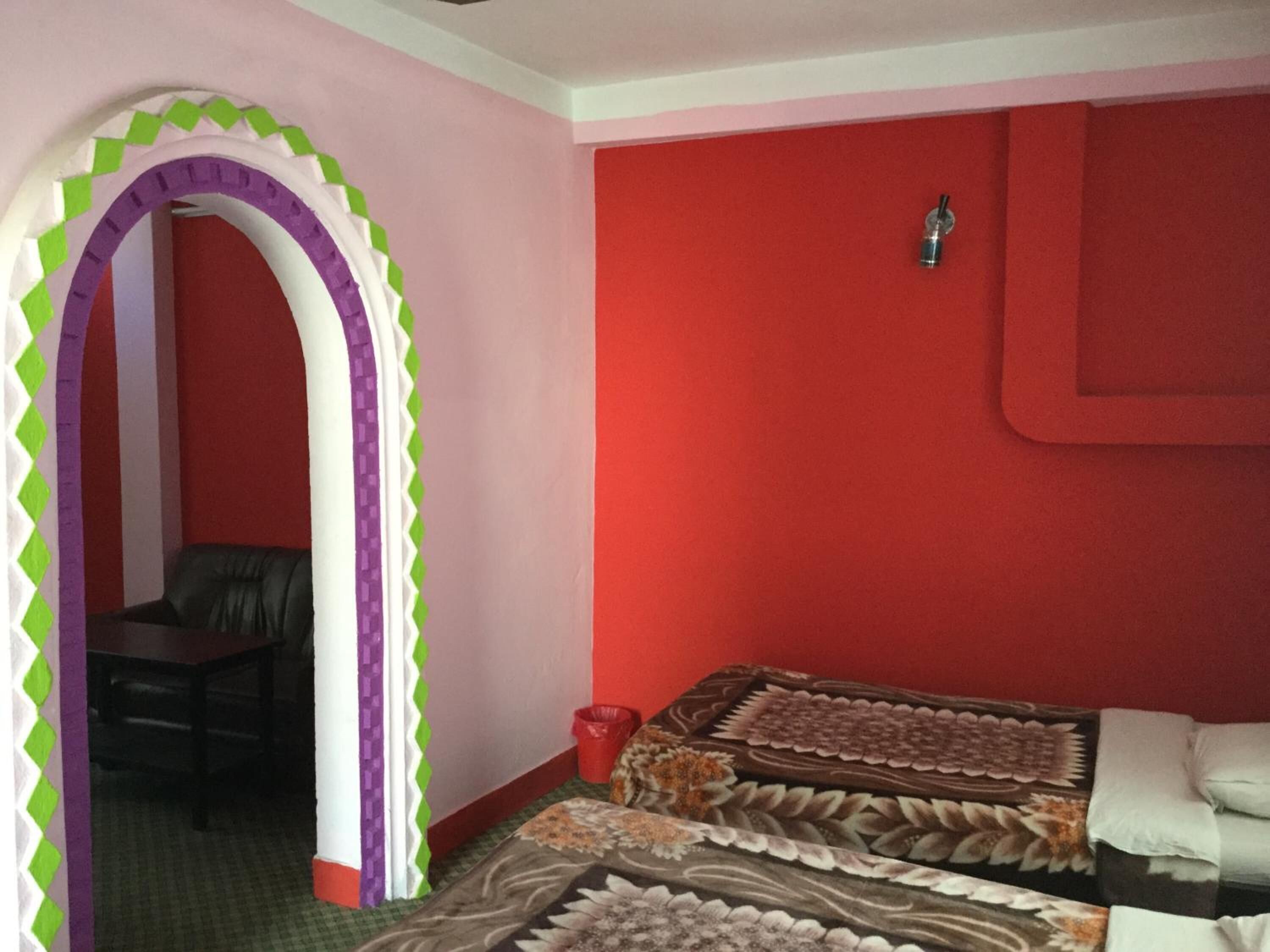 A room with two beds, a red wall, a small table, and a chair.