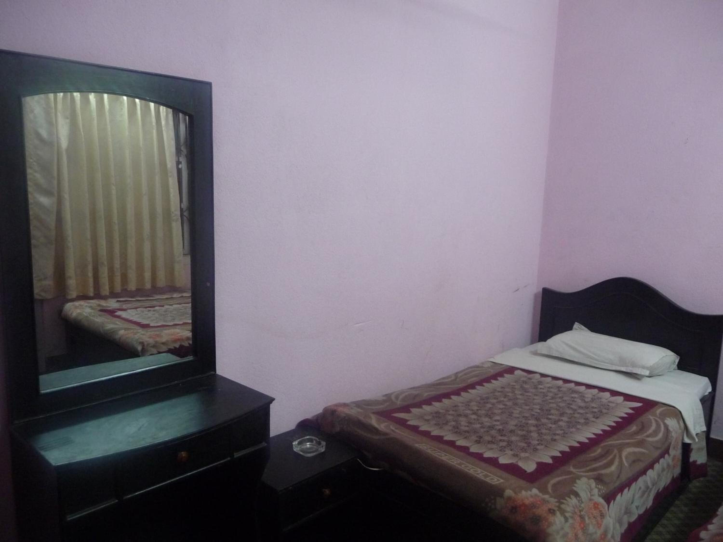 A bedroom with a bed, a bedside table, a dresser, and a mirror.