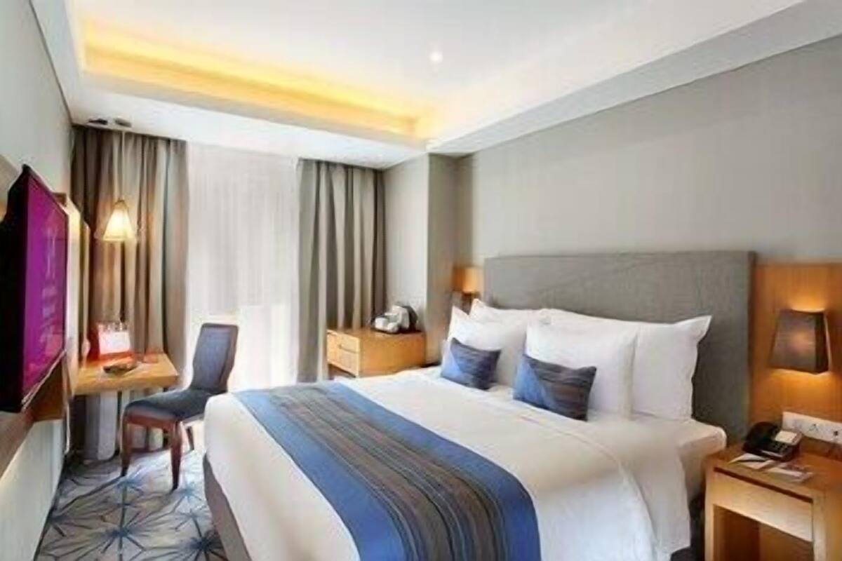A hotel room with a bed, a desk, a chair, a TV, and a lamp.