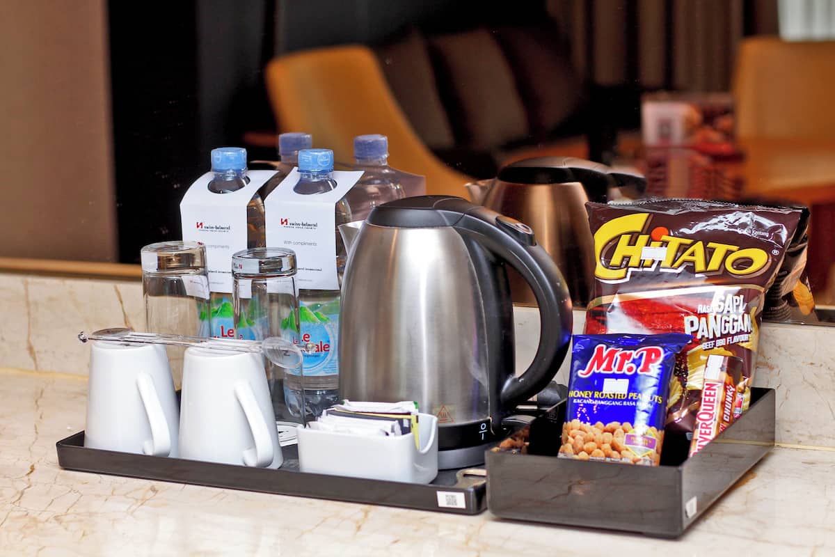 A kitchen counter with a coffee maker, water bottles, a kettle, and snack packages.