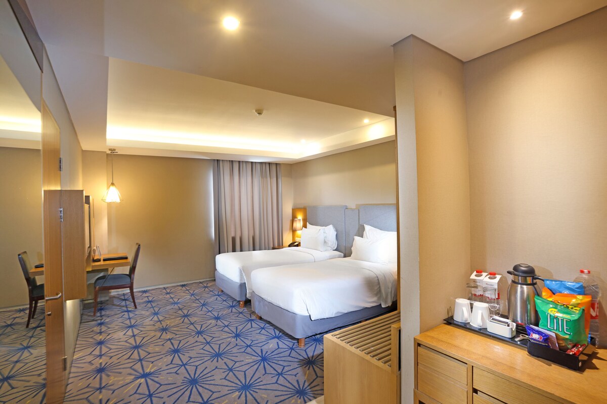 Habitación de hotel con dos camas, un escritorio, una silla y un minibar.