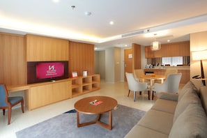 A modern hotel room with a wooden entertainment unit, a round coffee table, a sofa, a dining area with chairs, and a kitchen area. - Swiss-Belhotel Pondok Indah (Jakarta)