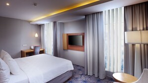 Habitación de hotel con una cama grande, un escritorio, una silla, un televisor y una ventana con cortinas.