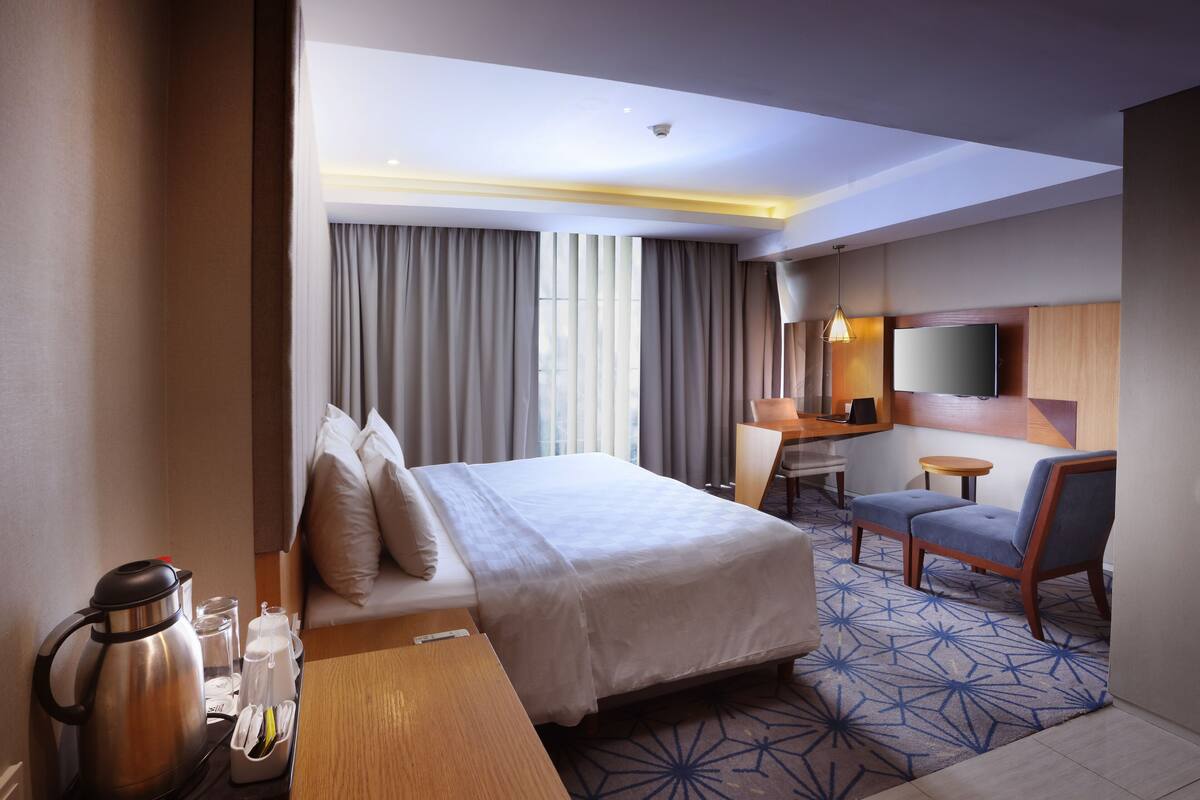 A hotel room with a bed, a desk, a chair, a TV, and a coffee maker.