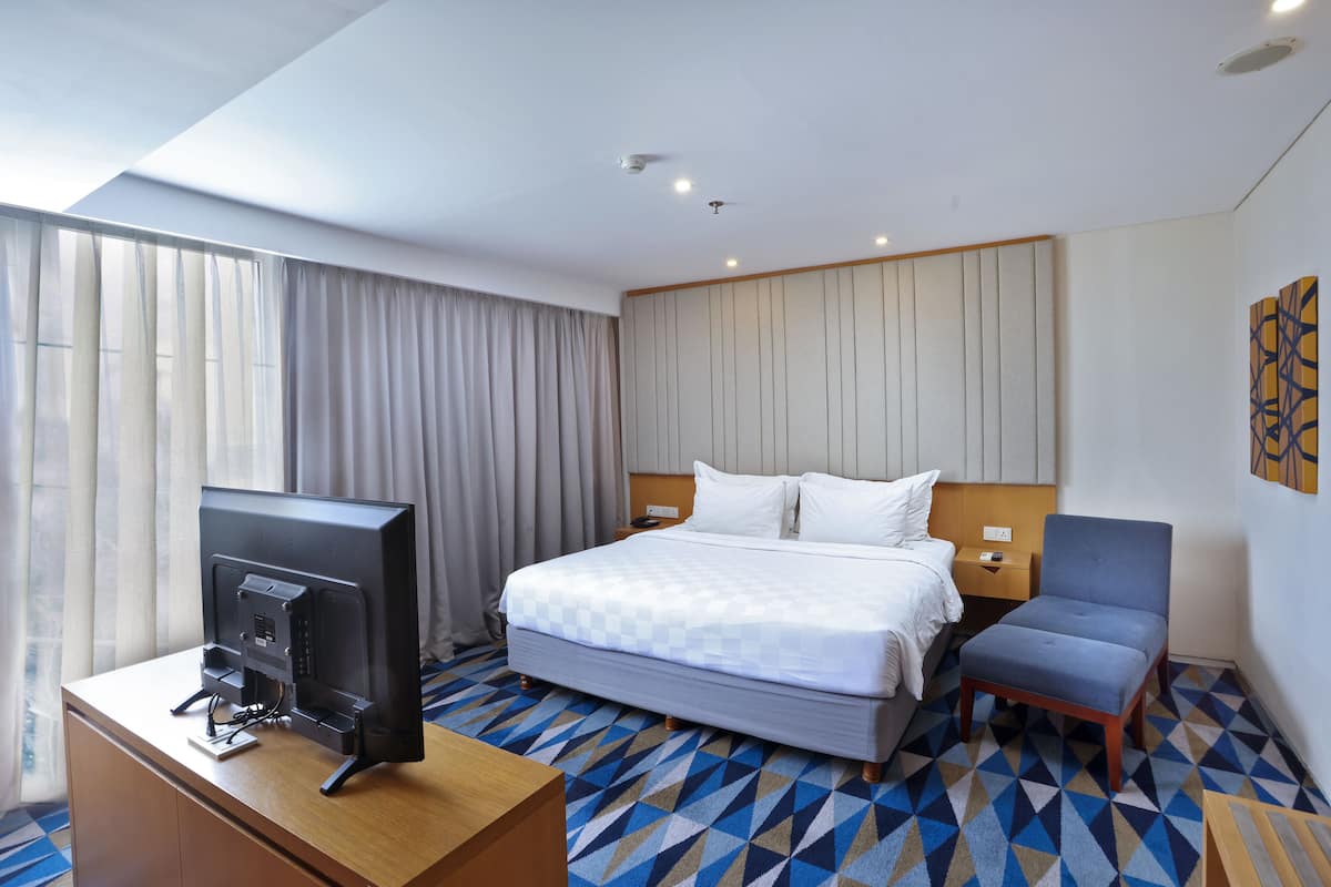 A hotel room with a bed, a desk with a computer, a chair, and a TV.