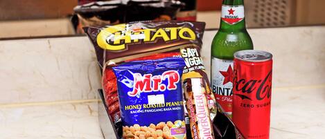 A snack box containing M&Ms, Silverbrown, and other snacks, along with a Coca-Cola can and a bottle of Bintang beer.