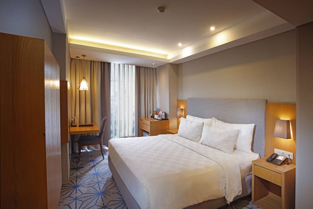 A hotel room with a large bed, bedside tables, a desk, and a chair.