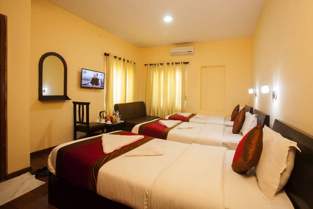 Habitación de hotel con tres camas, un televisor, un escritorio con silla y una ventana con cortinas.
