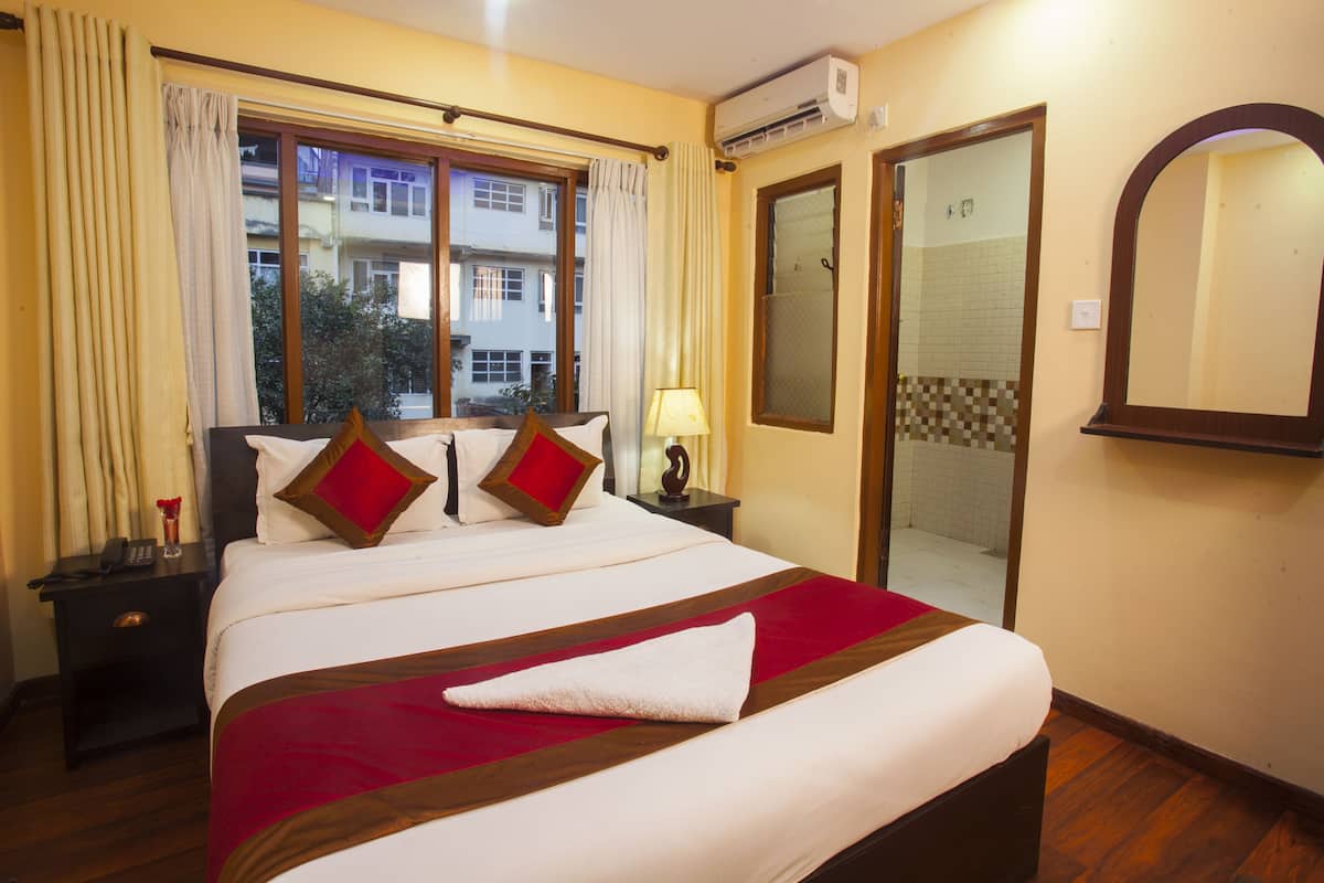Habitación de hotel con una cama grande, una mesita de noche con lámpara, una ventana con cortinas y una puerta corrediza de cristal que da a un balcón.