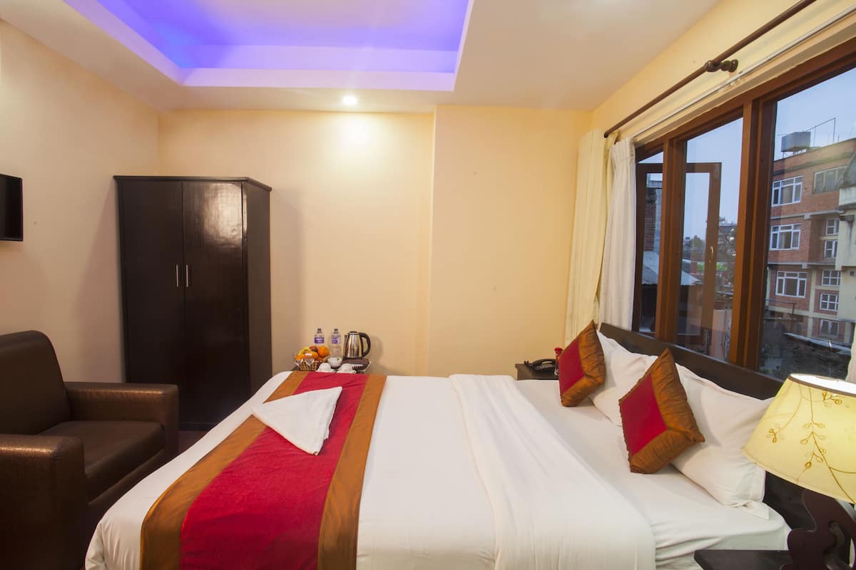 Una habitación de hotel con cama, armario, escritorio con lámpara y ventana con vista a edificios.