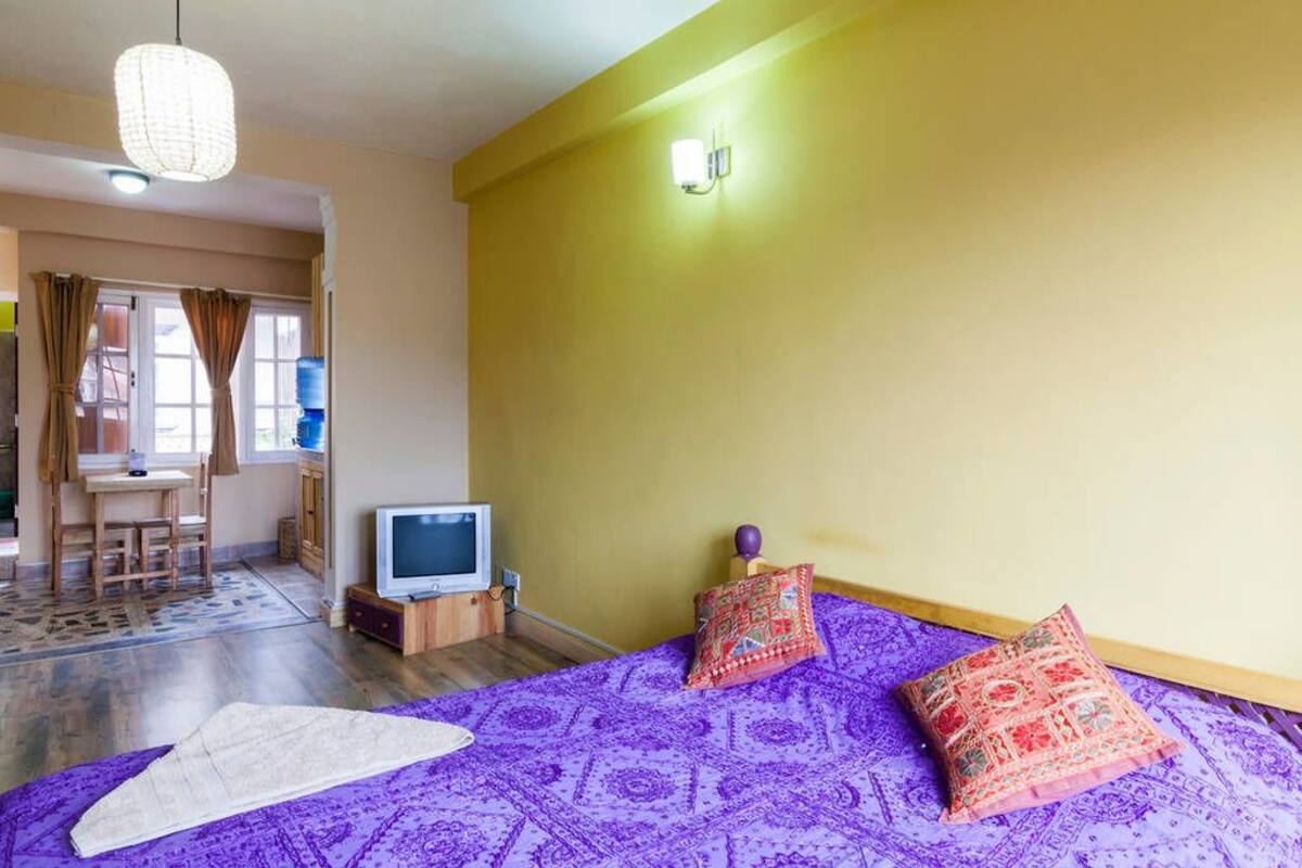 A room with a bed, a desk, a television, and a window with curtains.
