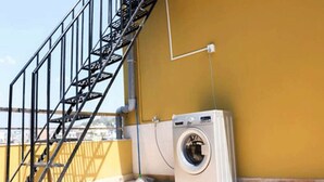Una lavadora en un balcón con una escalera metálica y una pared amarilla.