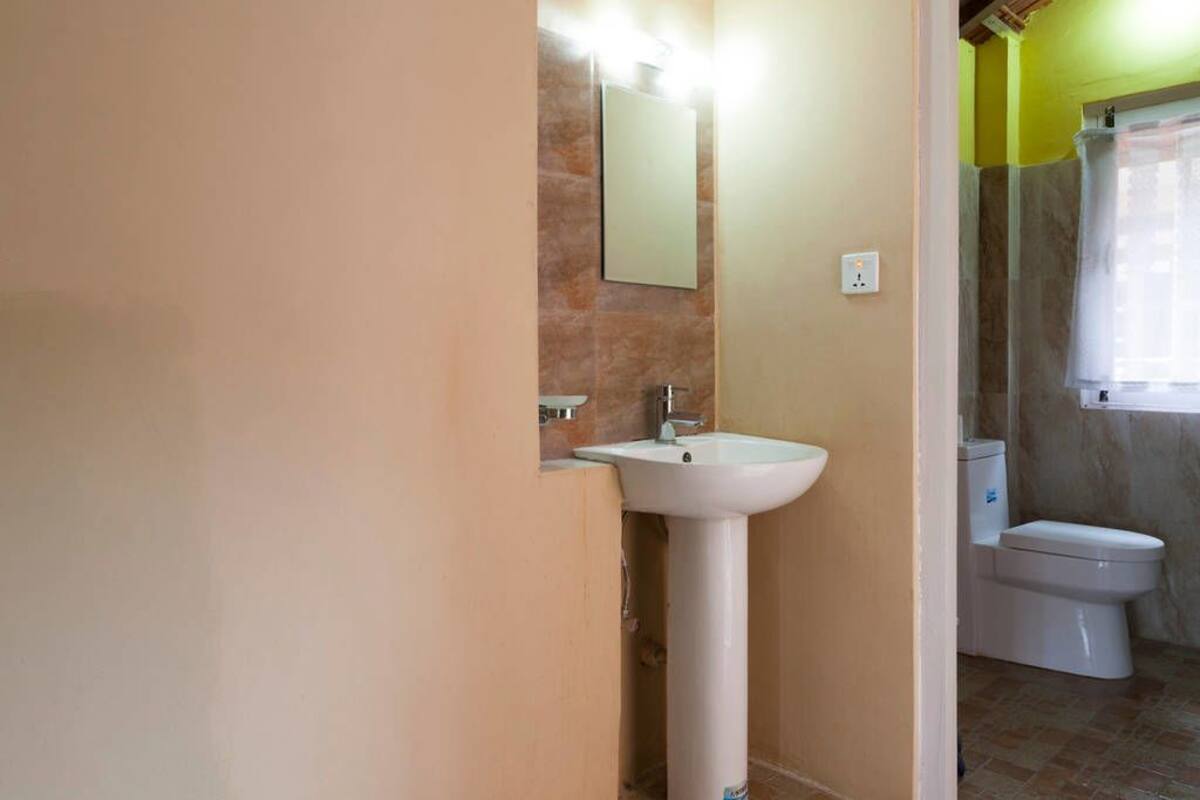 A bathroom with a pedestal sink, a mirror, a toilet, and a window with a shower curtain.