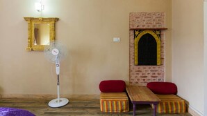 Una habitación con chimenea de ladrillo, un ventilador de pie, un espejo y dos bancos rojos acolchados.
