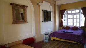 Una habitación con cama, mesa, banco, calefactor y ventana con cortinas.