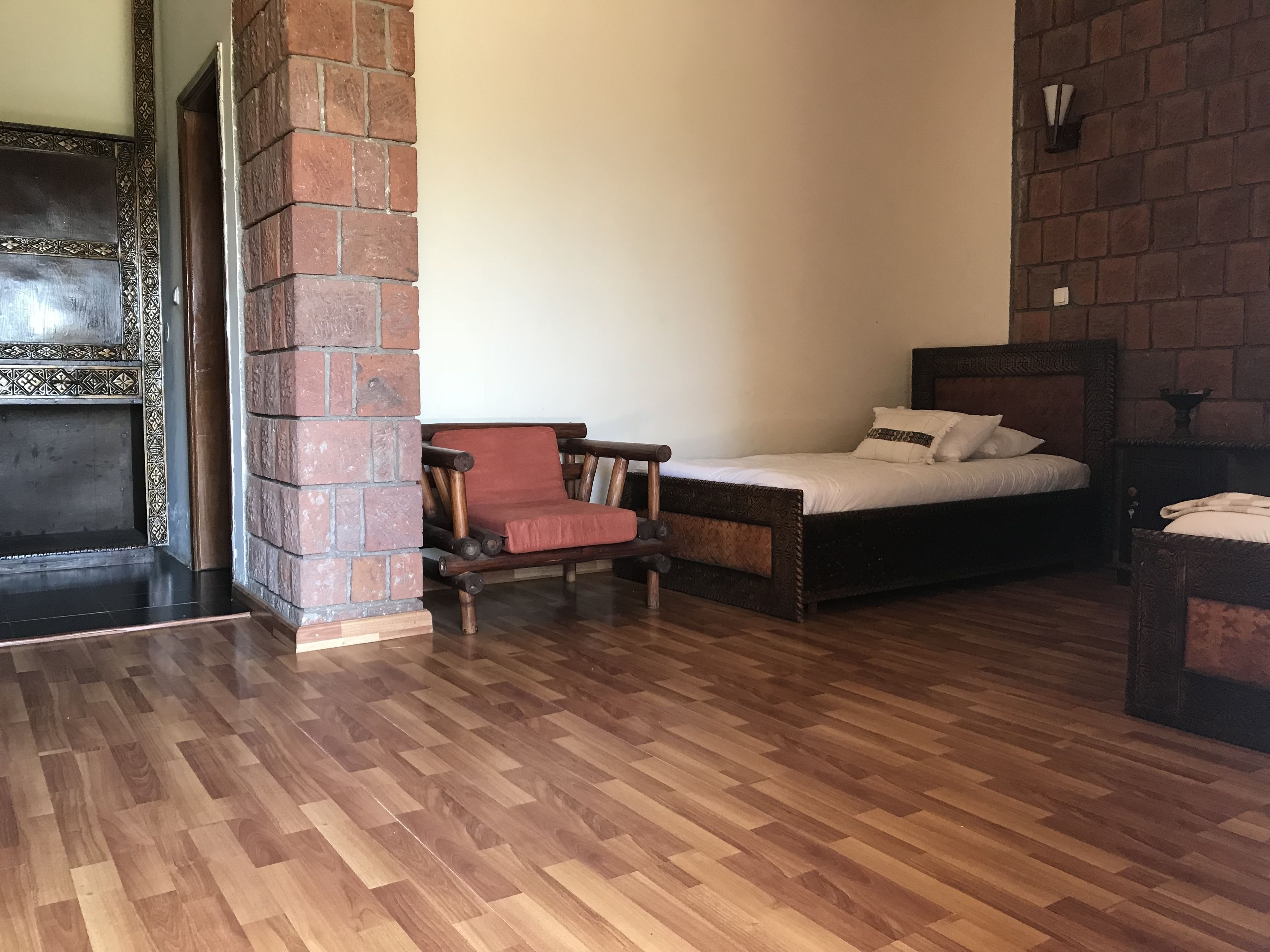 Una habitación con piso de madera, pared de ladrillo, una cama con cabecera y una silla de madera.