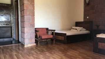 Una habitación con piso de madera, pared de ladrillo, una cama con cabecera y una silla de madera.