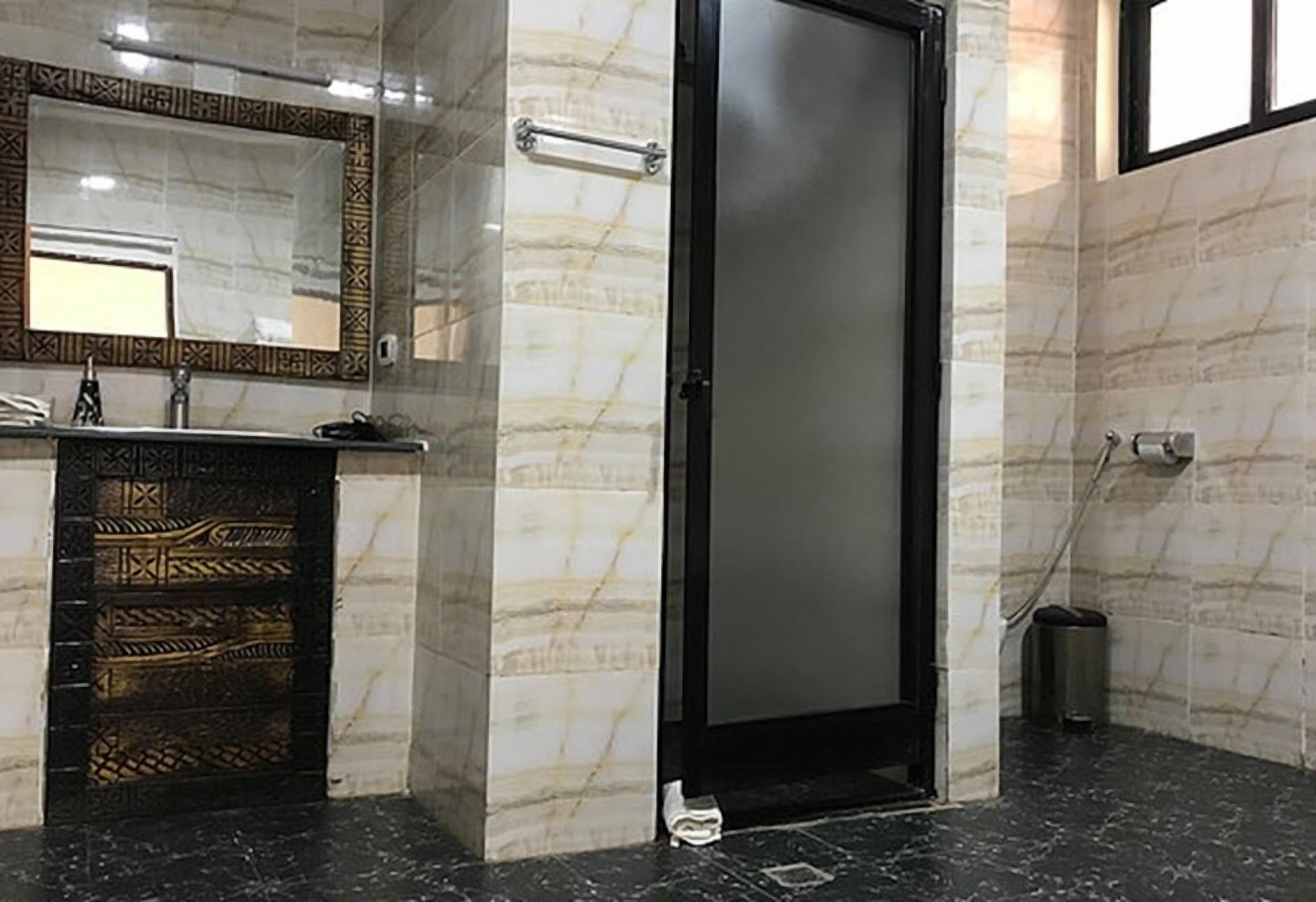 A modern bathroom with a marble wall, a black door, and a hand dryer.