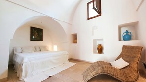 A room with a bed, a wicker chair, and shelves with vases. - La Fuggiola (San Vito dei Normanni)