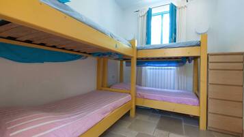 Cozy single-room accommodation with a bunk bed setup and a single bed, featuring a simple layout and a window with curtains.