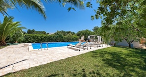 Ein Swimmingpool mit Liegestühlen und einer Pergola, umgeben von einem gepflegten Rasen und Bäumen.