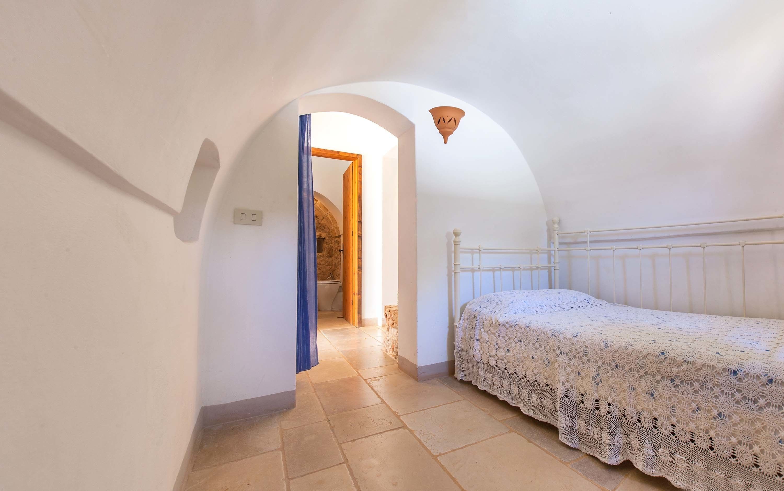 Un pasillo estrecho y arqueado que conduce a un dormitorio con una cama blanca y una lámpara decorativa en el techo.