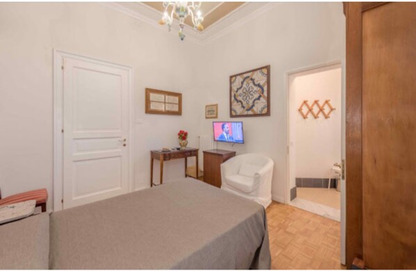 Un dormitorio con cama, escritorio, silla, televisor y puerta.