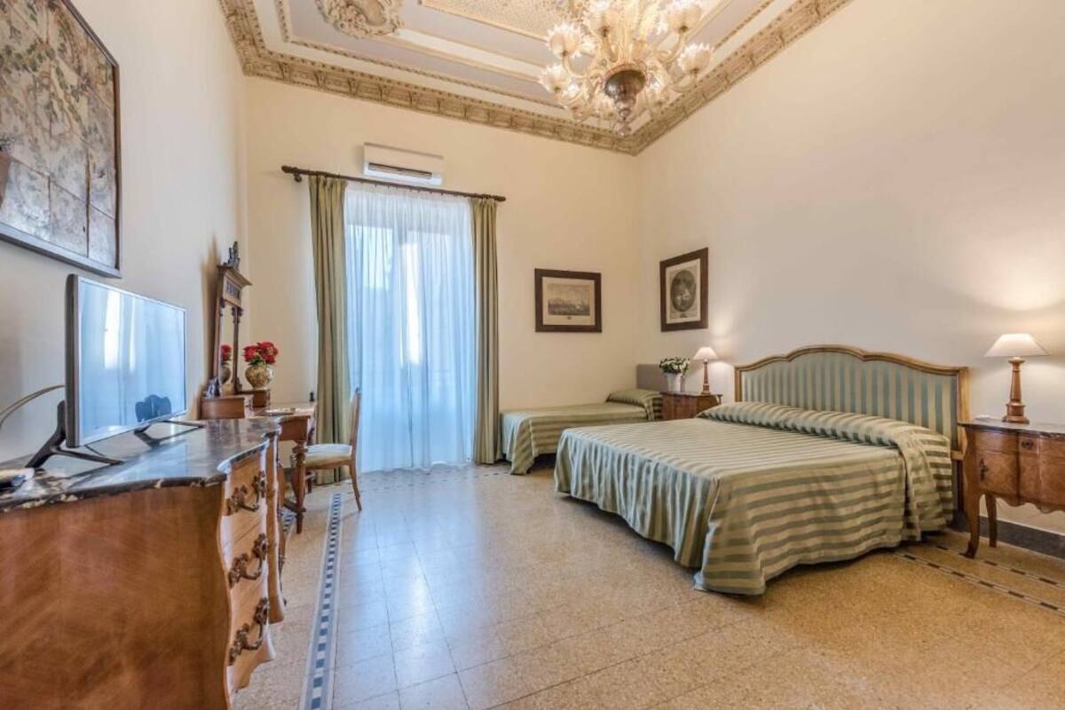A hotel room with a bed, a desk, a chair, a television, and a chandelier.