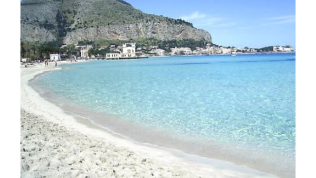 A beach with clear turquoise water, a sandy shore, and a rocky hill in the background. - B&B Palazzo Benso (Palermo)