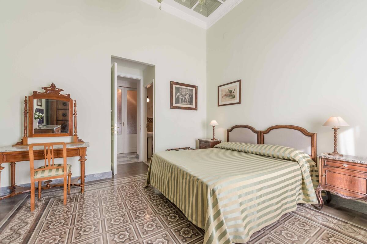 A bedroom with a bed, a wooden dresser, a nightstand, a mirror, and a chair.