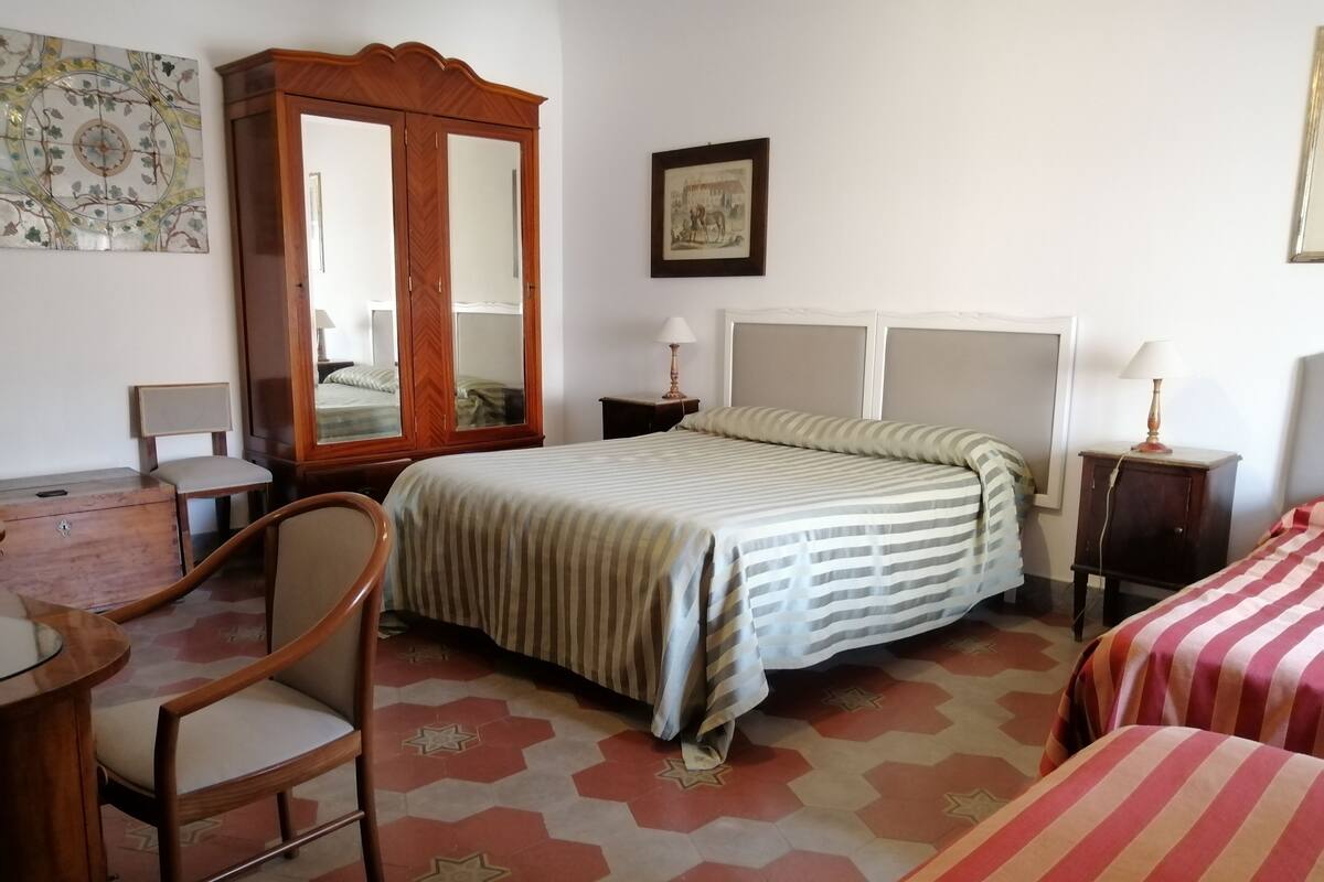 A bedroom with a bed, a wooden wardrobe, a desk, and a chair.