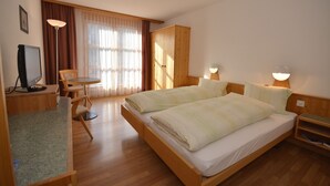 A hotel room with a wooden bed, a desk with a computer, a chair, and a large window with curtains.
