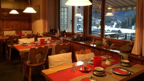 A dining area with wooden tables and chairs, red placemats, and a view of a snowy landscape through large windows.