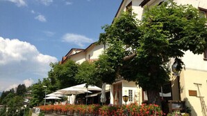 A two-story building with a stone facade, a large tree in front, and outdoor seating with umbrellas.