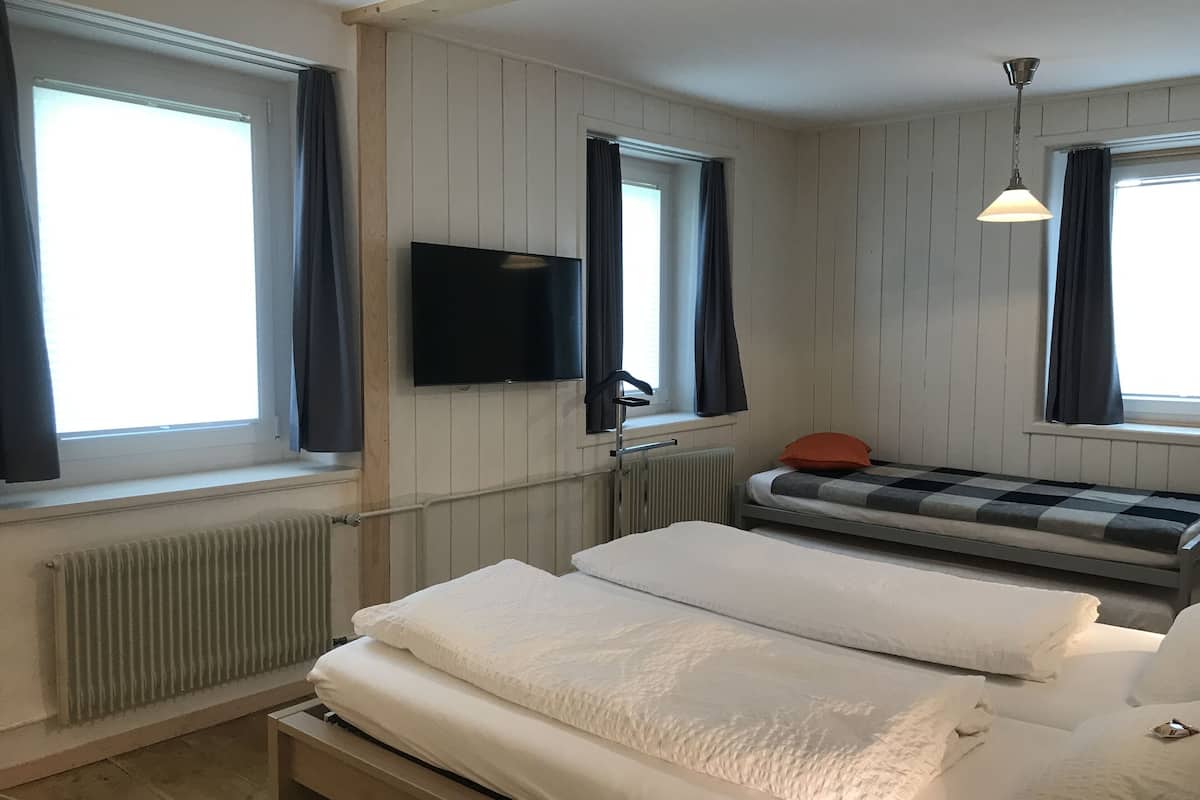 Una habitación con dos camas, un televisor instalado en la pared y un ventanal con cortinas.