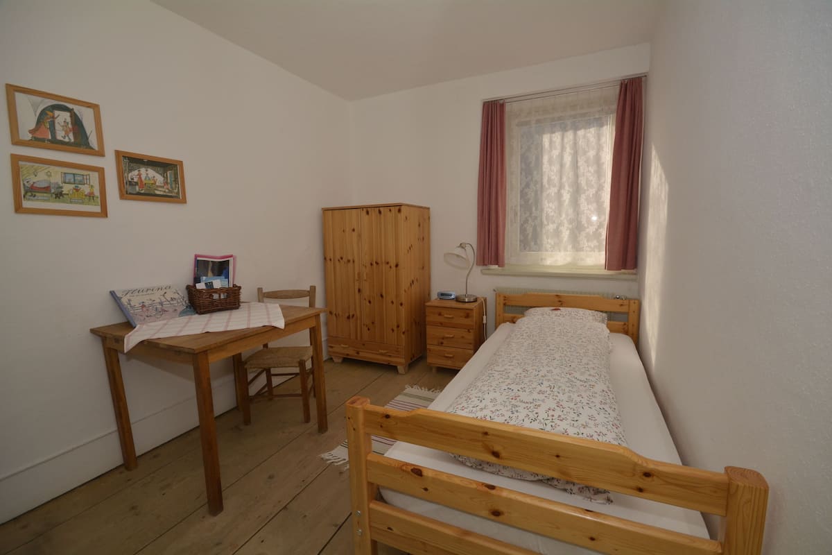 Un dormitorio con una cama de madera, un escritorio con una silla, un armario y dos cuadros en la pared.