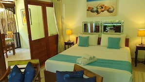 A hotel room with a bed, two bedside tables, a chair, a desk, and a painting on the wall. - Maison Soleil (Mahé Island)