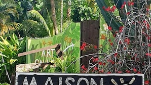 A sign for a self-catering guest house and art gallery named Maison Soleil, with a tropical garden background. - Maison Soleil (Mahé Island)