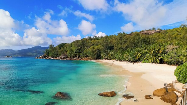 A beach with clear turquoise water, a sandy shore, and lush green vegetation. - Maison Soleil (Mahé Island)