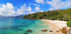 A beach with clear turquoise water, a sandy shore, and lush green vegetation. - Maison Soleil (Mahé Island)