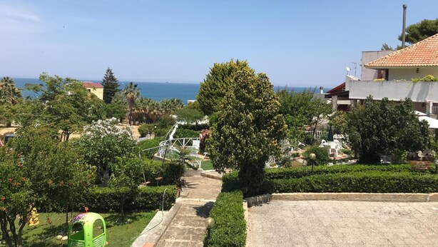 Zona residencial con vista al mar, una silla verde y un camino que lleva a un edificio con techo de tejas.