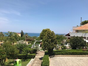 Zona residencial con vista al mar, una silla verde y un camino que lleva a un edificio con techo de tejas.