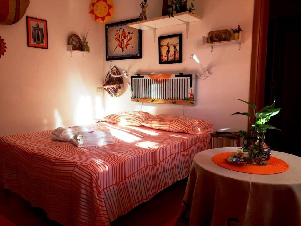 Un dormitorio con una colcha a rayas, una mesita de noche con una lámpara y estantes en la pared con objetos decorativos.