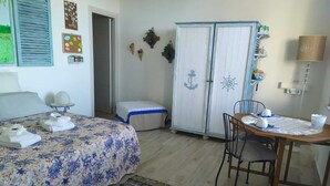 Un dormitorio con cama, mesitas de noche, un armario, una mesa de comedor con sillas y una pequeña mesa con lámpara.