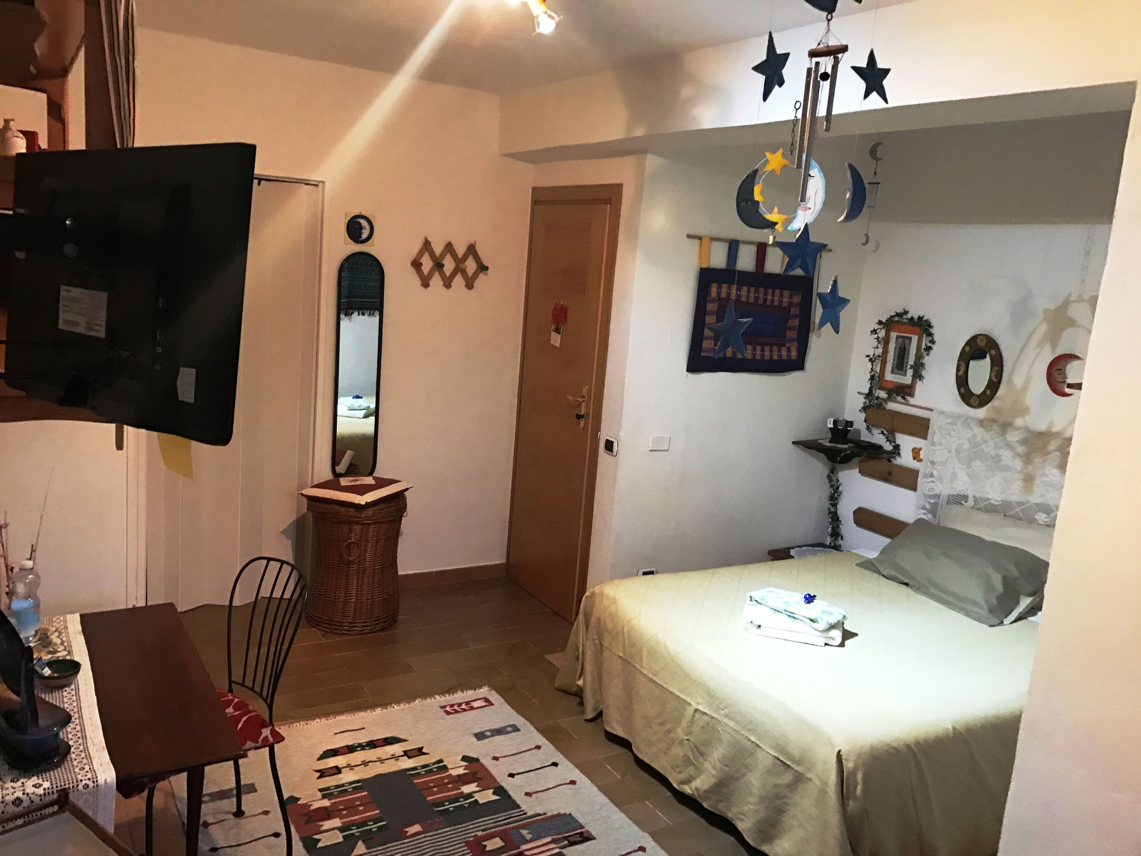A bedroom with a bed, a chair, a TV, a mirror, and wall decorations including stars and a crescent moon.